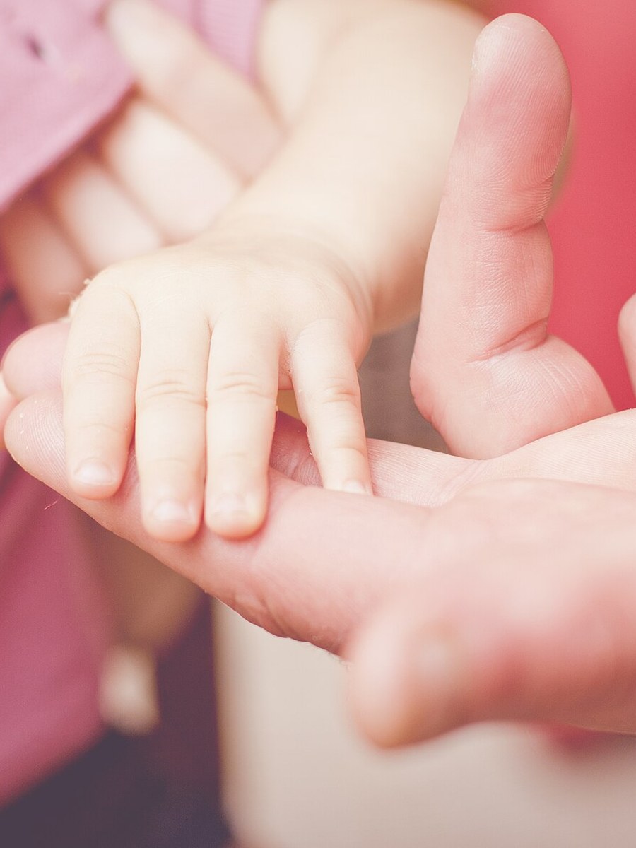 A small child's hand resting in an adult's open palm, lit by soft warm light